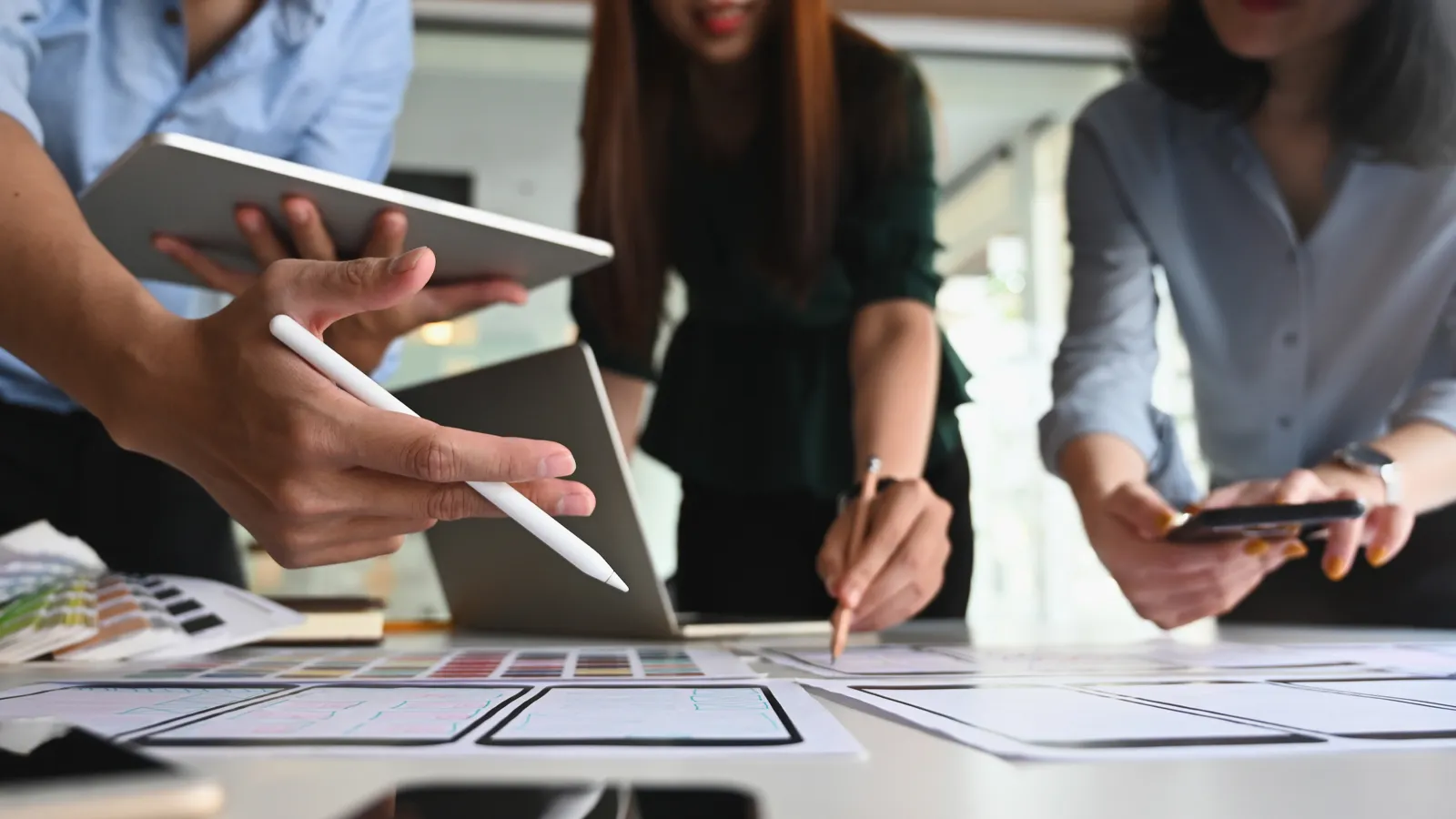 A picture of 3 people working on a design project together. Checking various mobile devices to make sure the design works.